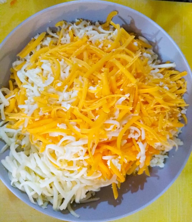 Shredded Monterey Jack and Cheddar cheeses in gray bowl with yellow background