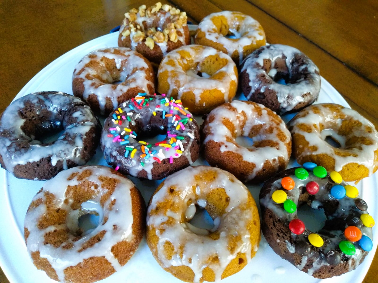 An iced assortment of fresh baked doughnuts. Some have walnuts, or sprinkles, or candy.