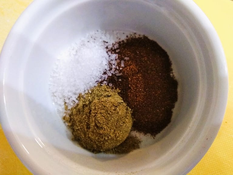 brown cumin powder, red chili powder, and salt in white bowl with yellow background