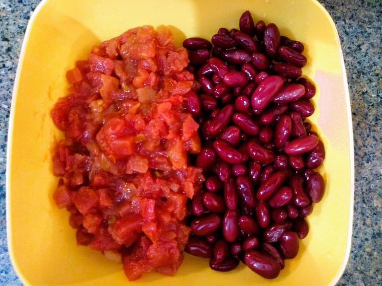 diced tomatoes and dark red kidney beans side by side in yellow bowl with granite background