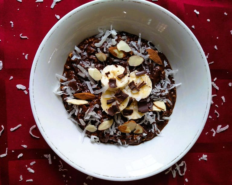 Garnished chocolate oatmeal with bananas, shredded coconut, and sliced almonds